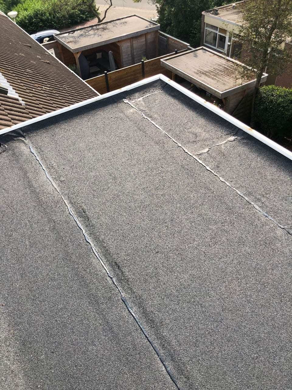Nieuw bitumen dak met een aluminium daktrim, van bovenaf gezien, met daaronder tuinen en schuren