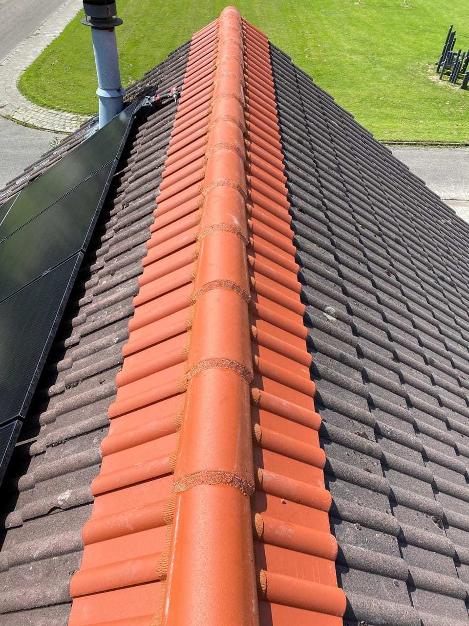 Pannendak met nieuwe oranje nokvorsten naast zonnepanelen