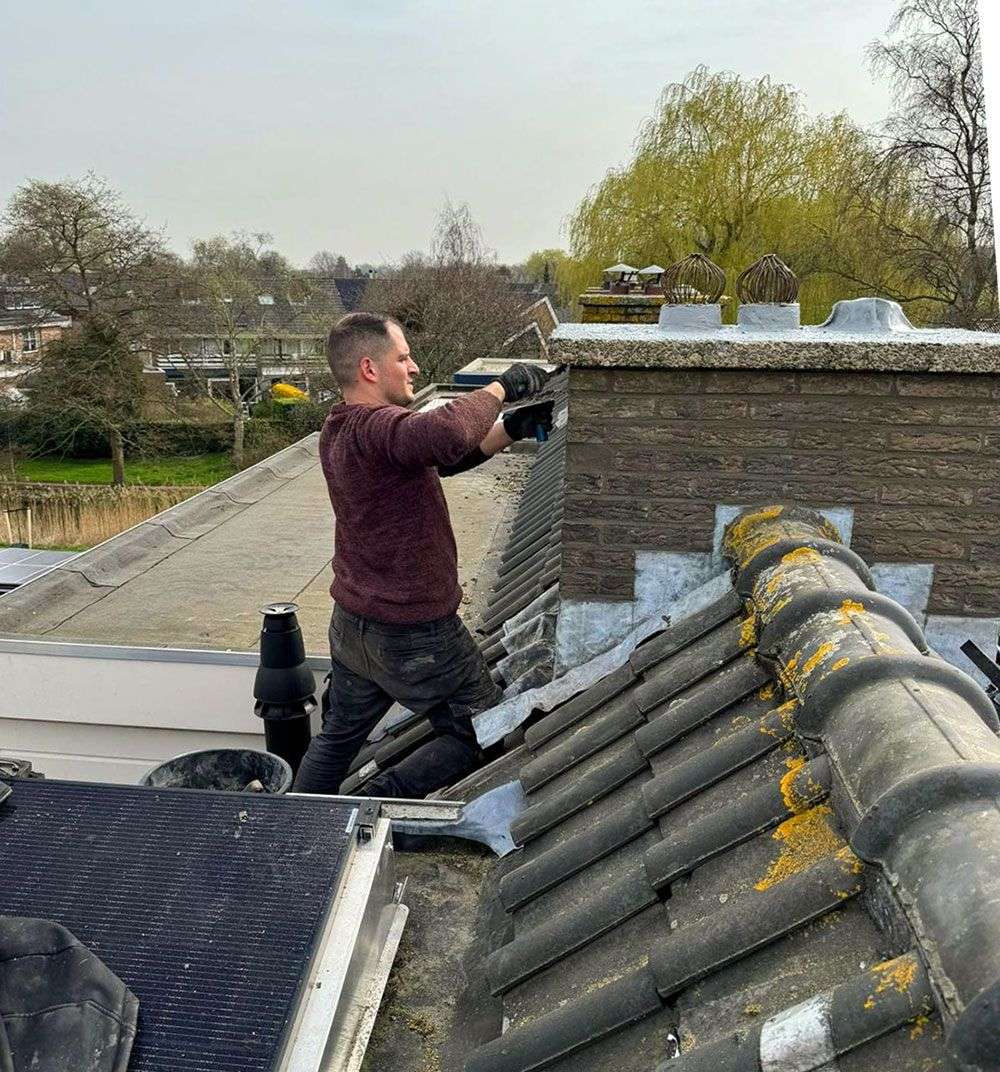 Dakdekker werkt aan een schoorsteen met nieuw lood op een pannendak